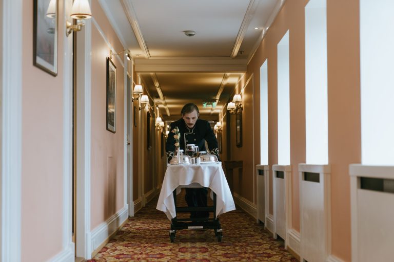 Hotel staff member quietly delivering room service through an elegant luxury corridor, illustrating discreet hospitality.